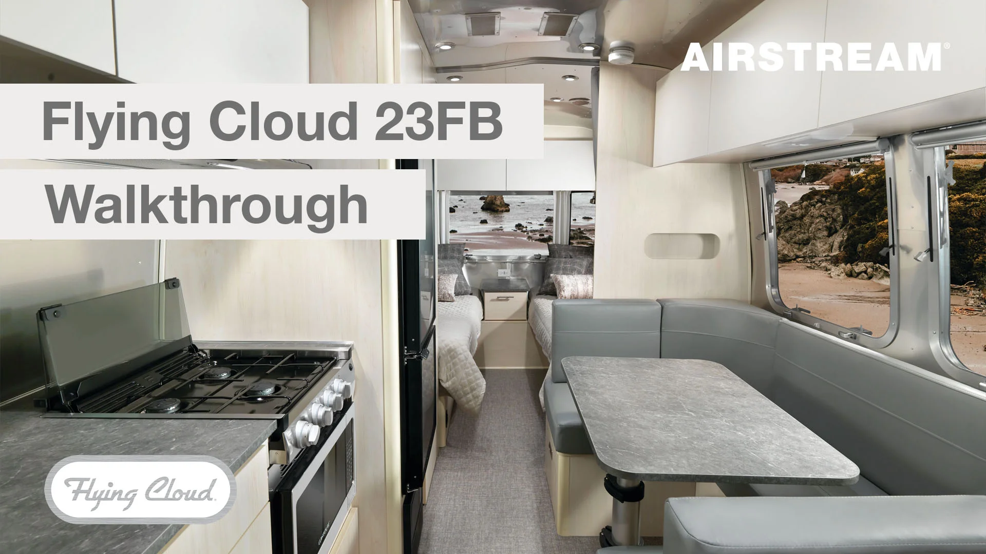 Interior of an Airstream Flying Cloud 23FB, featuring a dining area, kitchen with stove, and twin beds. Scenic landscape visible through windows.