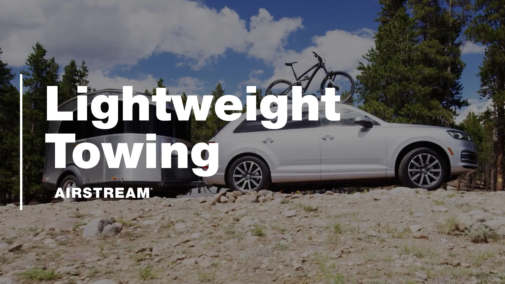 White car towing an Airstream trailer on a rocky path, with "Lightweight Towing" text overlay. Bike mounted on car roof; forest in background.