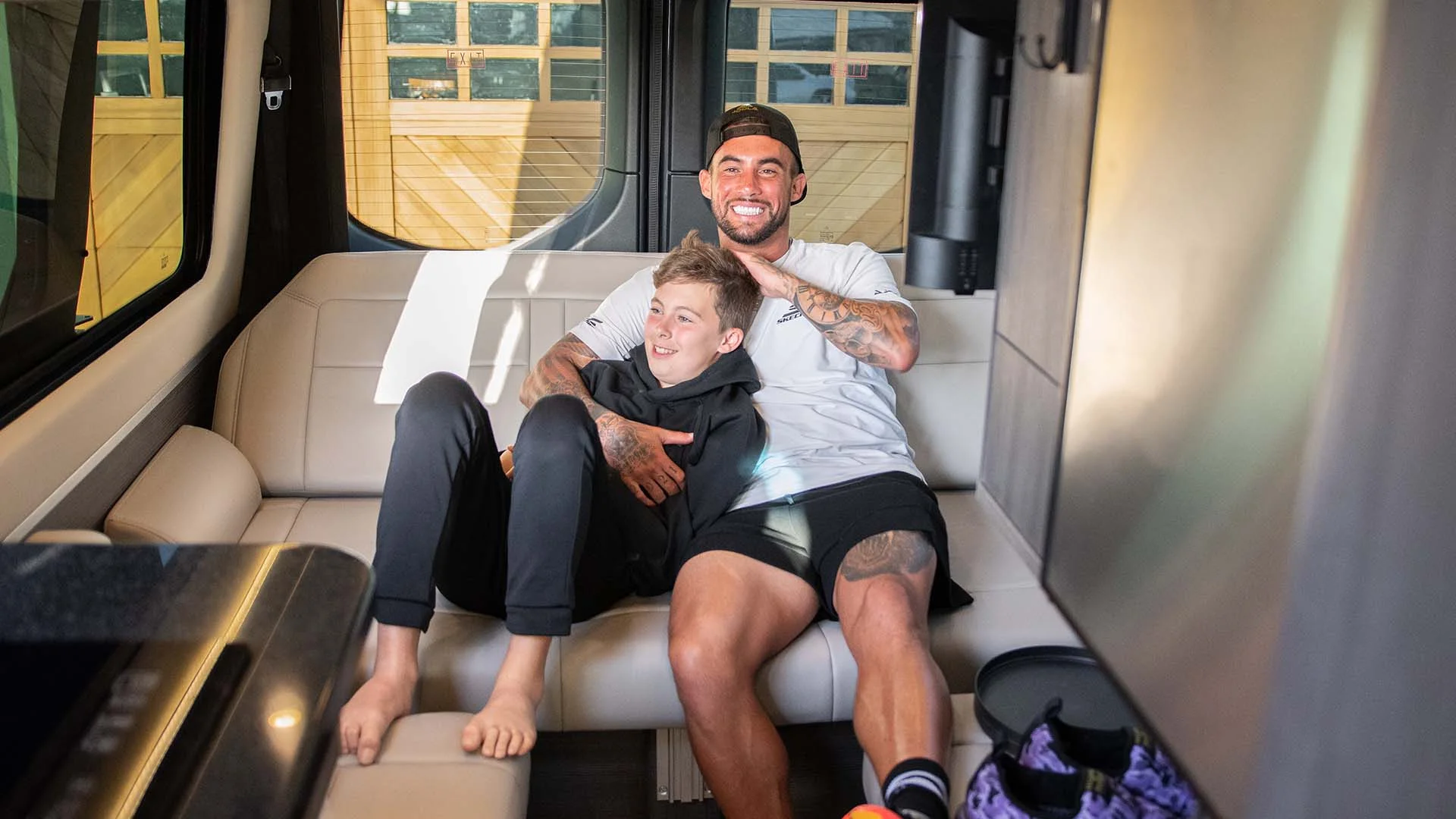 Two people smiling and sitting on a modern van sofa. One person has an arm around the other, creating a joyful and relaxed atmosphere.
