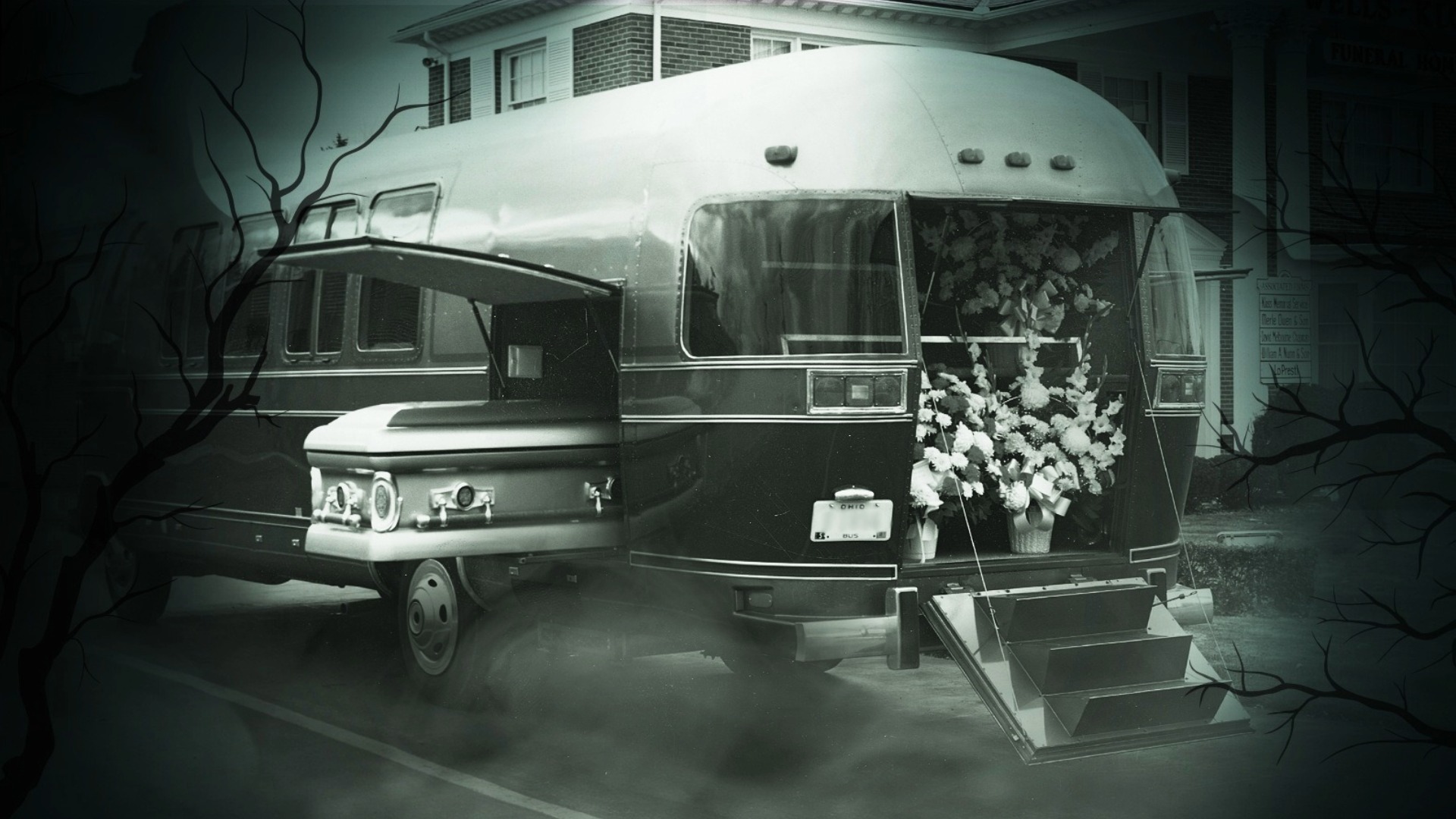 A vintage hearse with a casket inside and floral arrangements at the rear in a ghostly, foggy setting with bare tree branches.