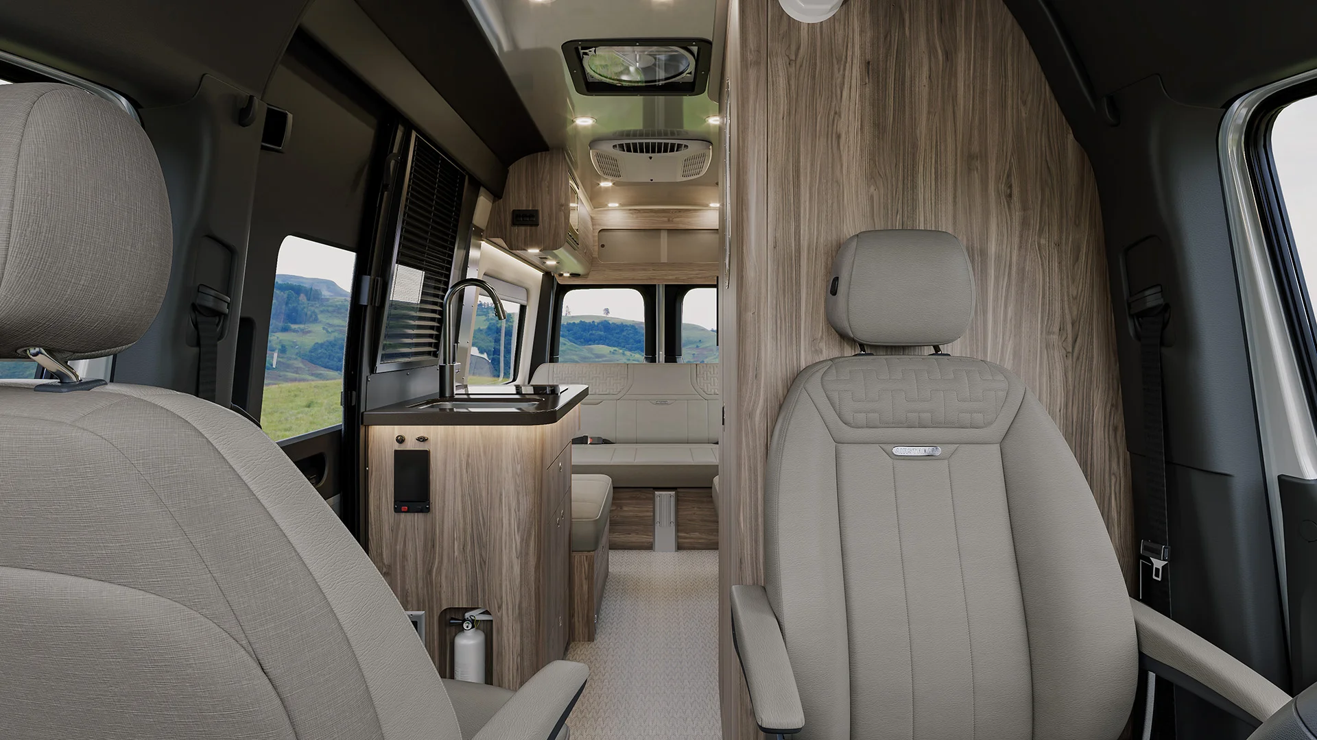 Interior of a modern camper van with beige seats, wood accents, a kitchenette, and a couch, with scenic views through the window.