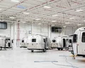 A spacious factory floor with several silver travel trailers positioned for assembly, featuring high ceilings and overhead lighting.