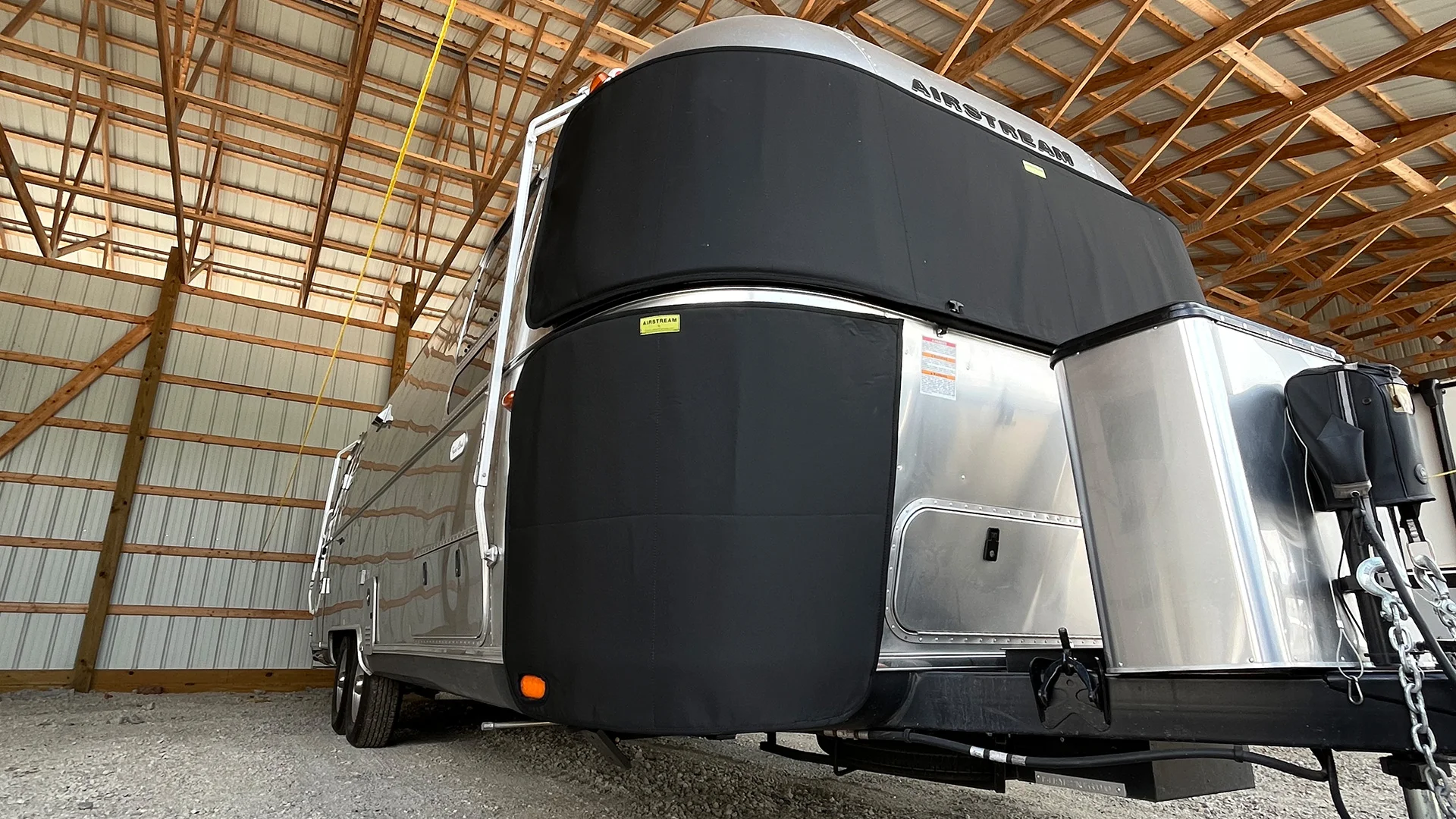 An Airstream trailer parked inside a wooden barn structure for storage.