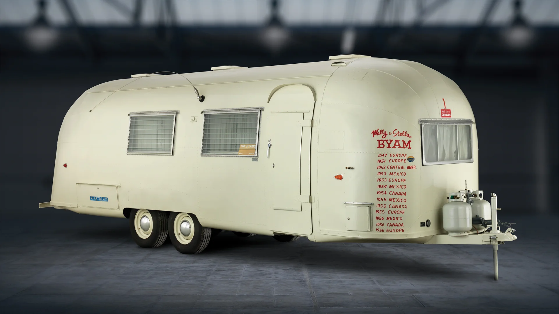 Vintage Airstream trailer with travel locations and dates listed on the side, displayed in an indoor setting.