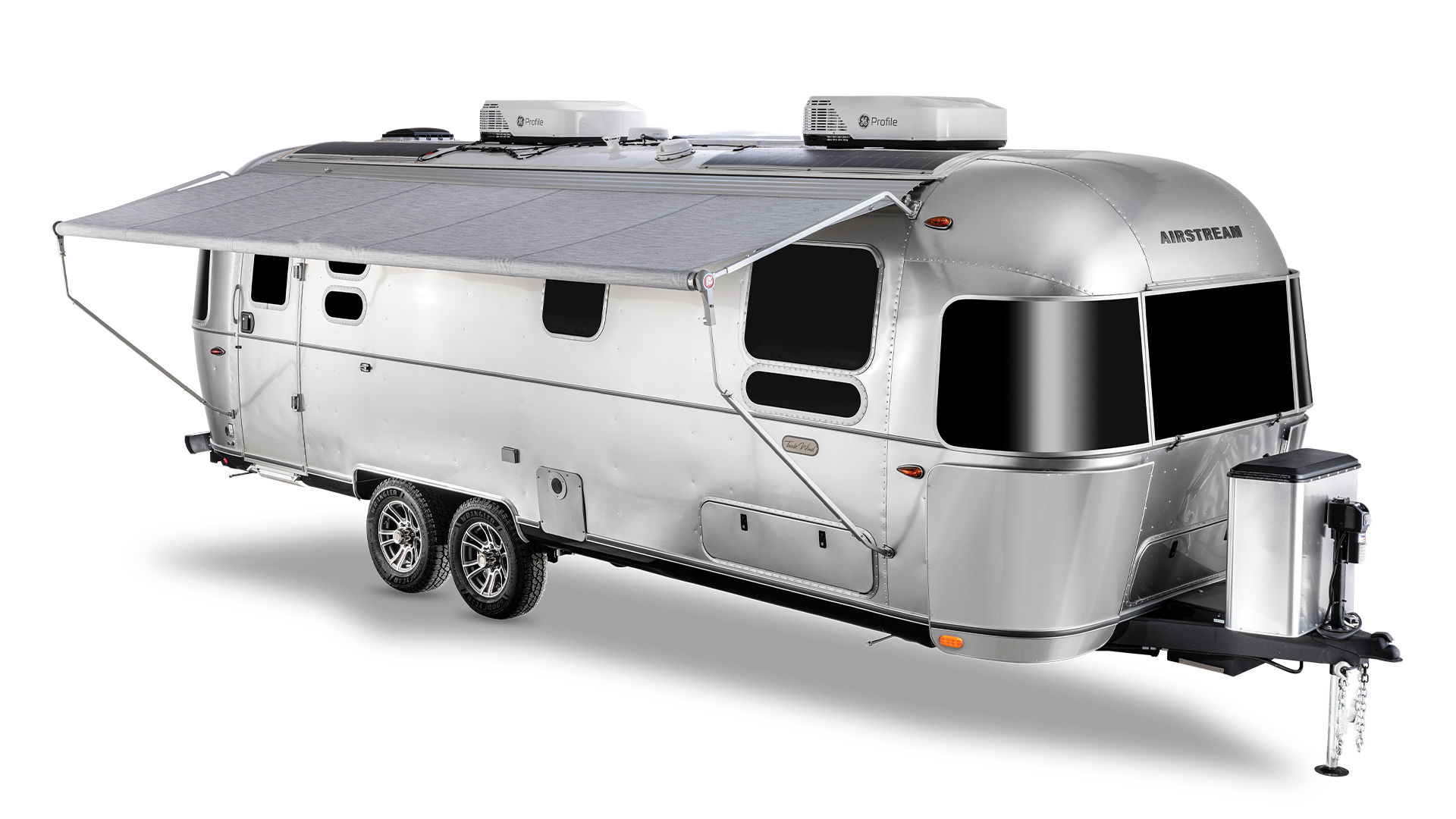 Sleek silver Airstream trailer with large windows, retractable awning, and dual axles.