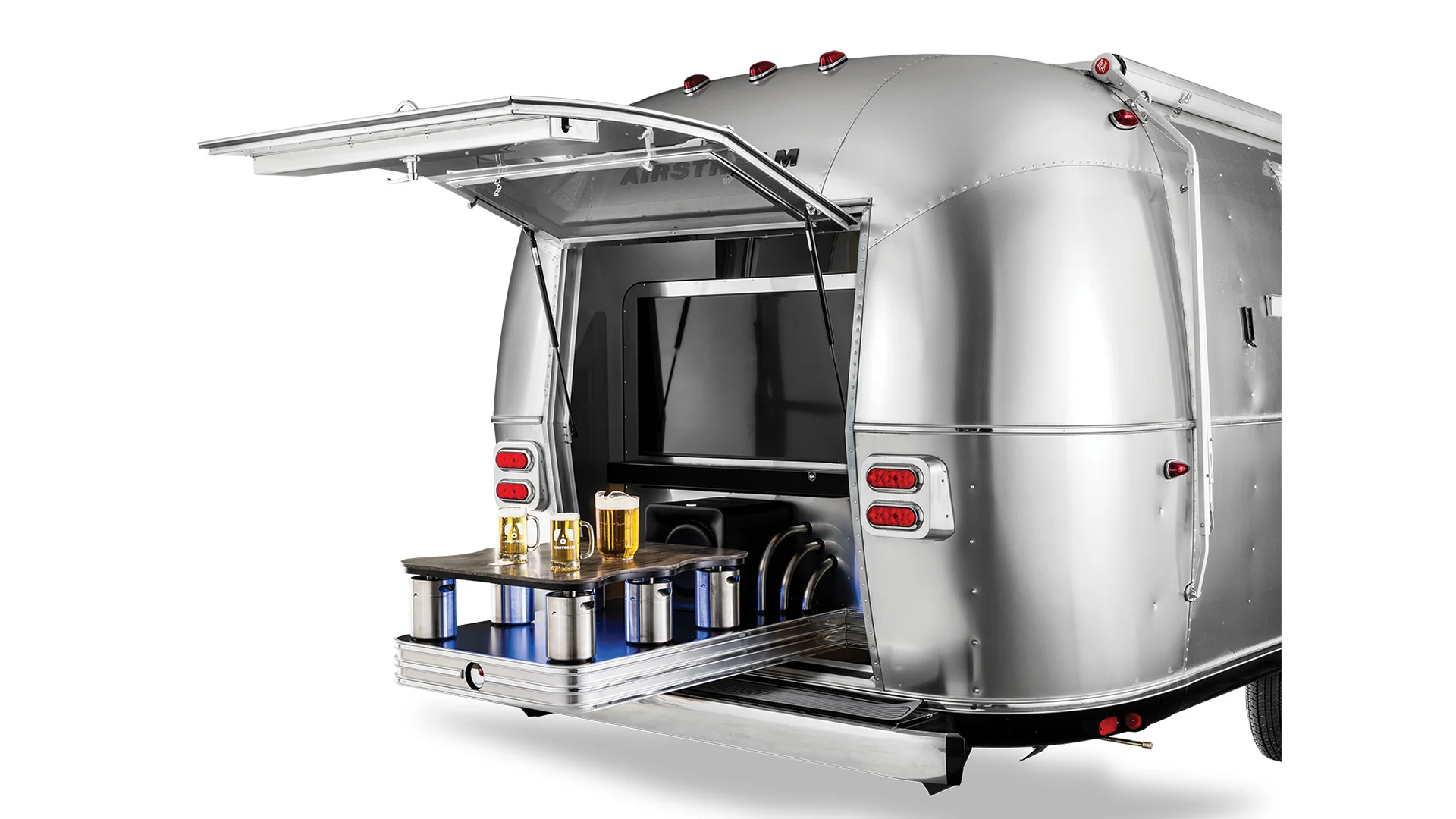 Airstream Commercial custom bar and beverage trailer with rear hatch open, revealing a built-in shelf holding beer mugs and containers. Tail lights and metallic finish are visible.