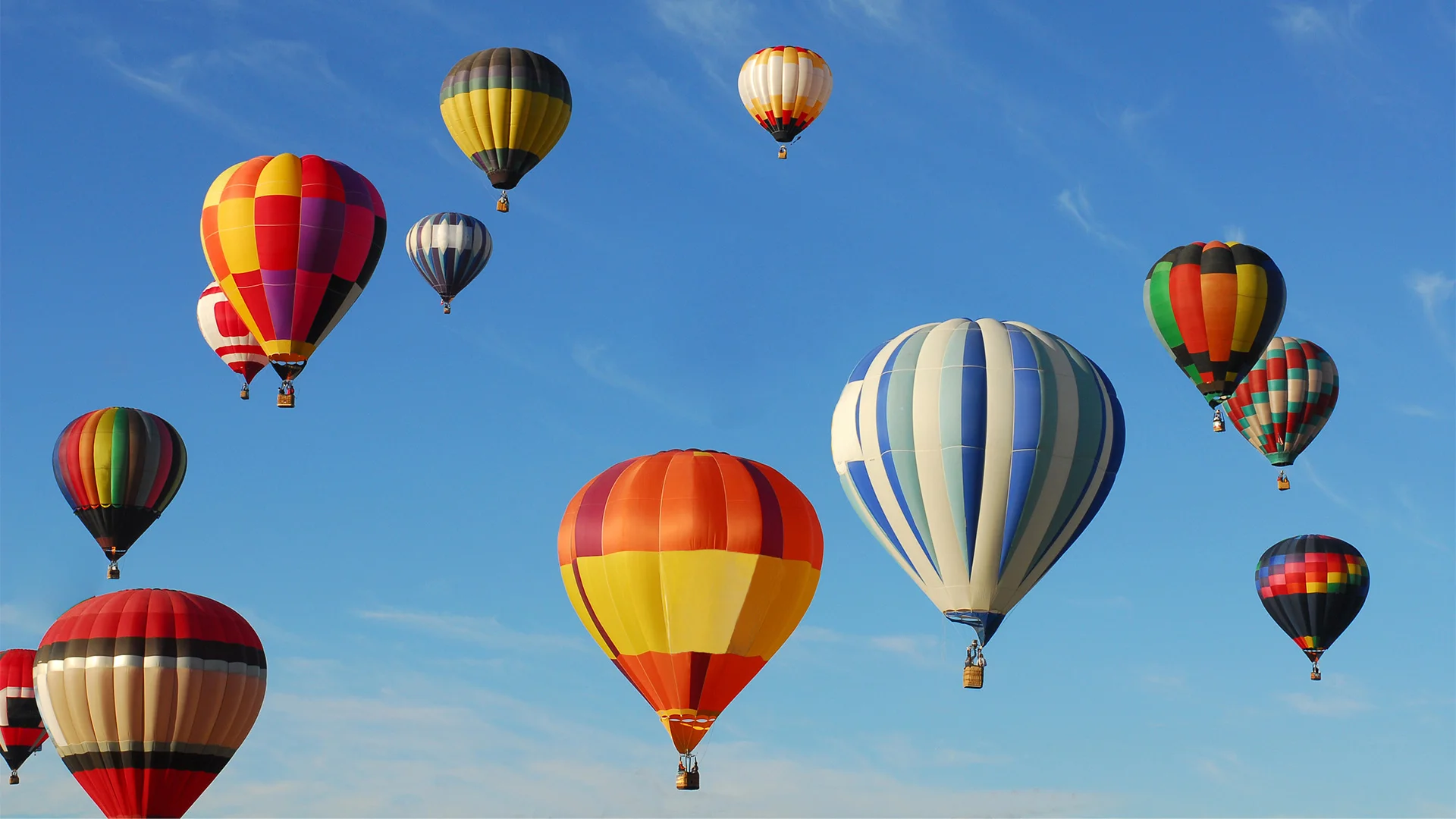 Colorful hot air balloons float against a clear blue sky, showcasing various patterns and stripes.