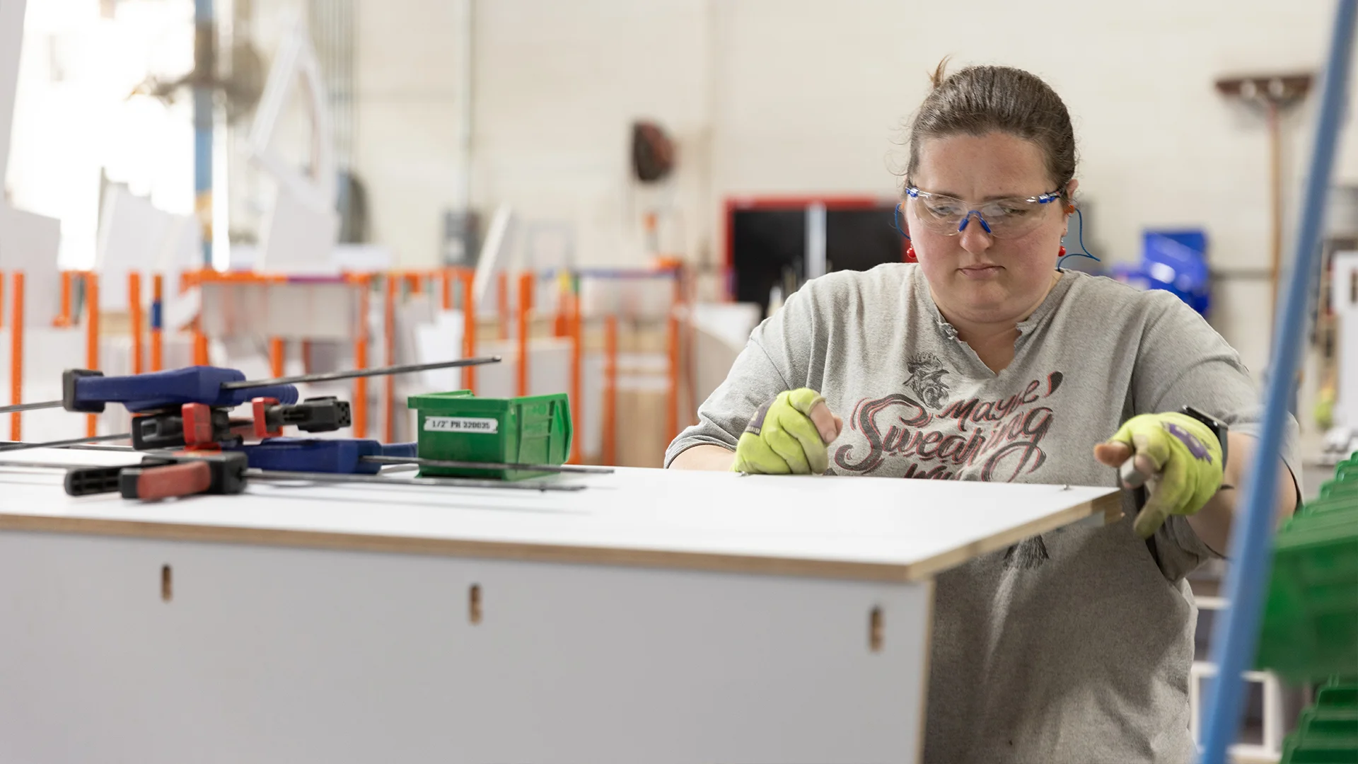 Person in safety goggles and gloves working on a piece of furniture in a workshop, with tools and clamps on the table.