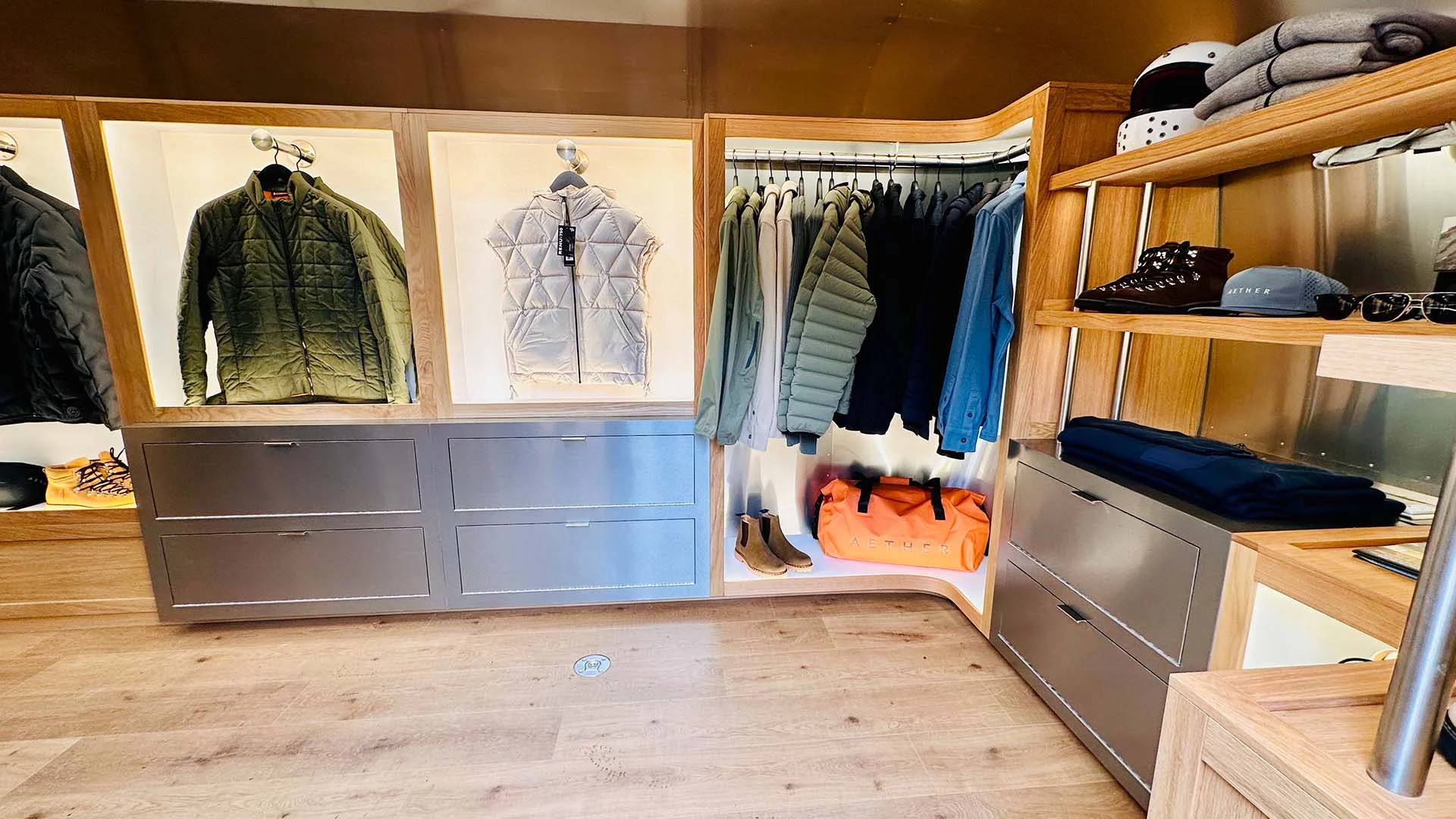 Modern closet with jackets, shirts, boots, and accessories on display. Bright lighting, wooden shelves, and a sleek, organized design.