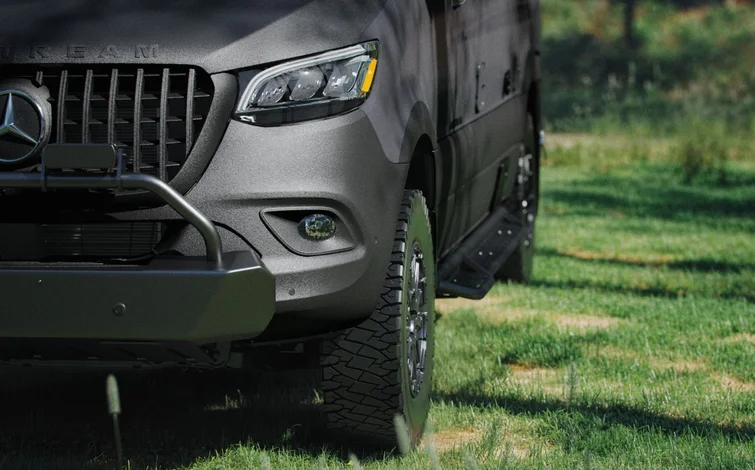 Close-up of a rugged black vehicle with large off-road tires parked on green grass.