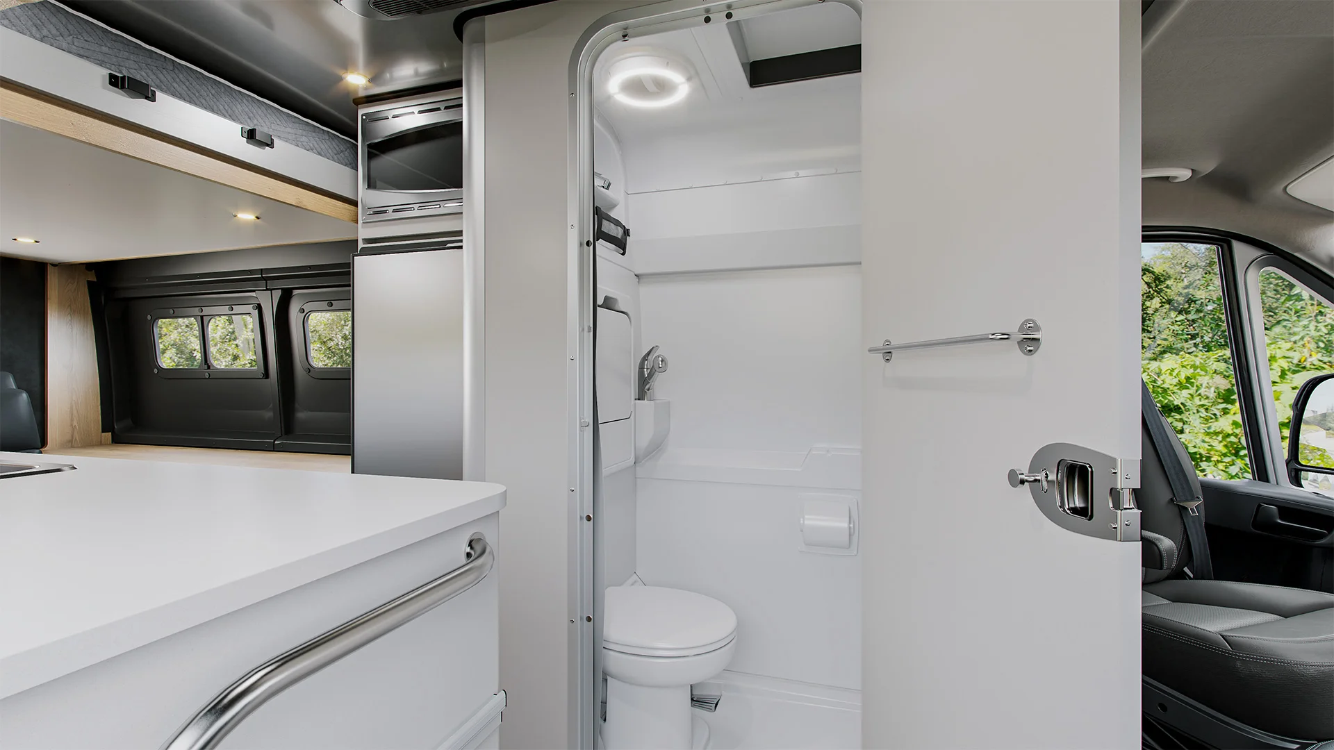 Interior of a modern RV bathroom with a toilet, sink, and shower. Adjacent kitchen area visible with sleek design and cabinets.