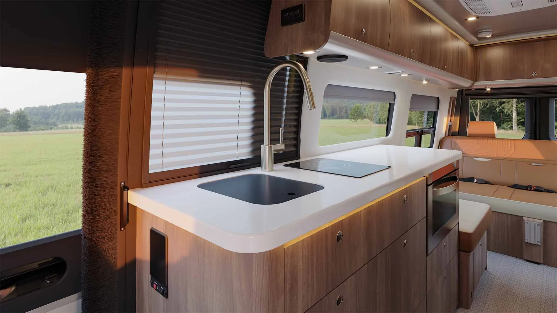Modern camper van interior with kitchenette featuring a sink, stovetop, and seating area. Large windows offer a scenic countryside view.