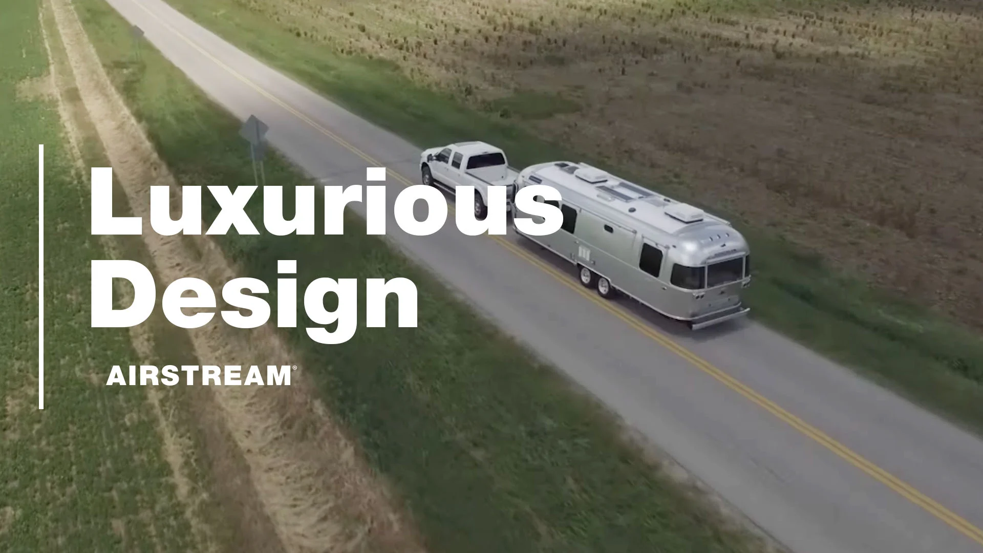 A white truck towing a silver Airstream trailer on a rural road, with text overlay saying "Luxurious Design AIRSTREAM."