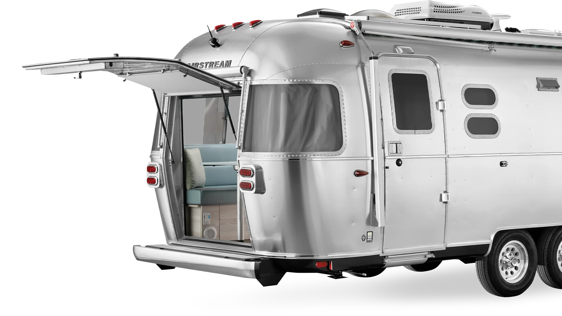 Silver Airstream trailer with open rear hatch, revealing a blue sofa and wooden interior, showcasing sleek design and portability.