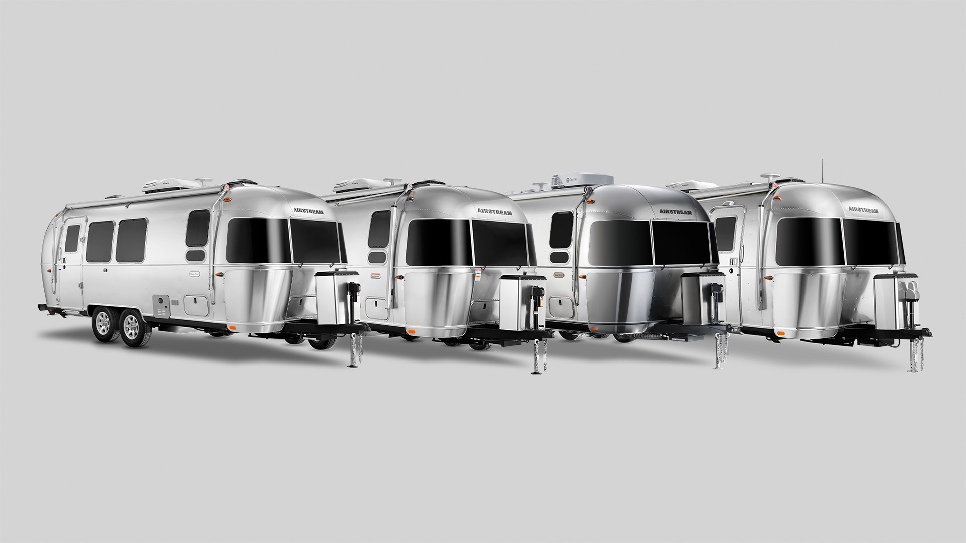 Four silver Airstream trailers lined up in a row on a neutral gray background.