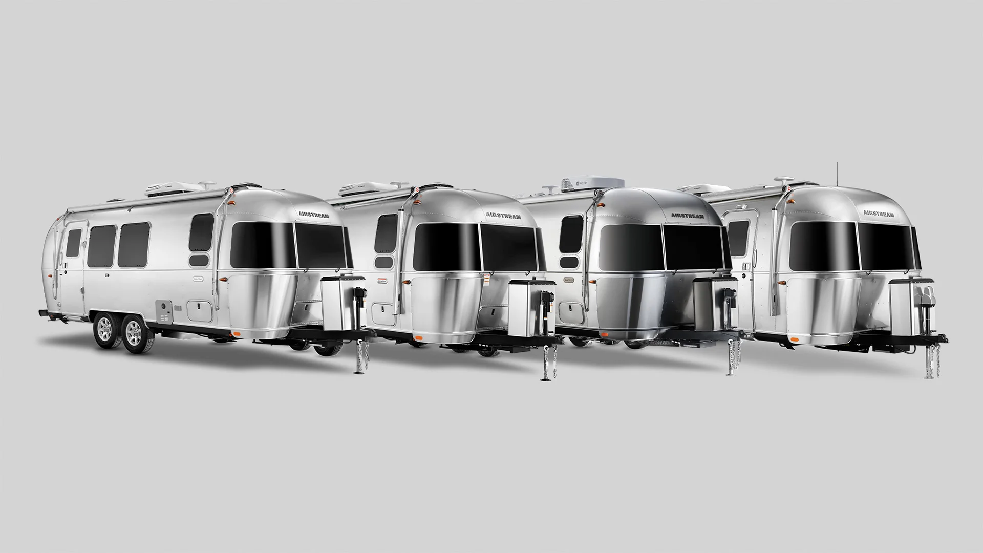 Four silver Airstream trailers lined up in a row on a neutral gray background.