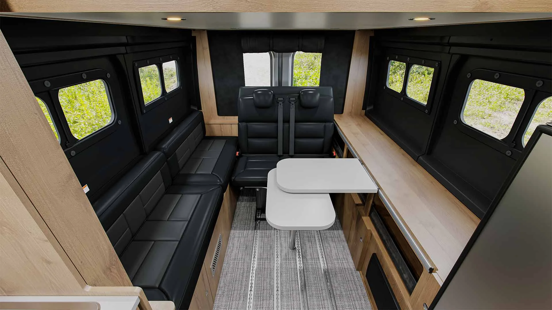 Interior of a camper van with black leather seats, a small foldable white table, wood paneling, several windows, and overhead lighting, creating a modern, cozy dining or sitting area.