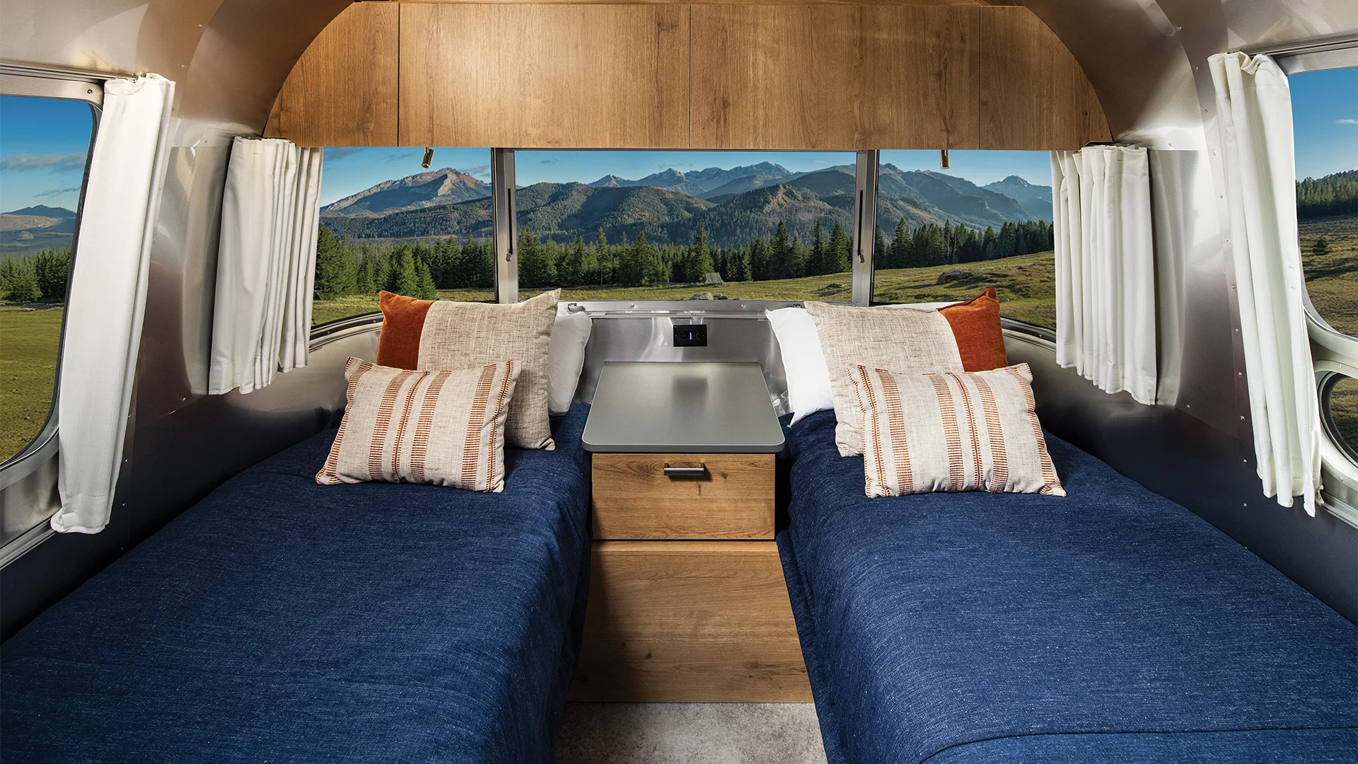 Interior of a camper with twin beds, wooden accents, and large windows showcasing a scenic mountain view.