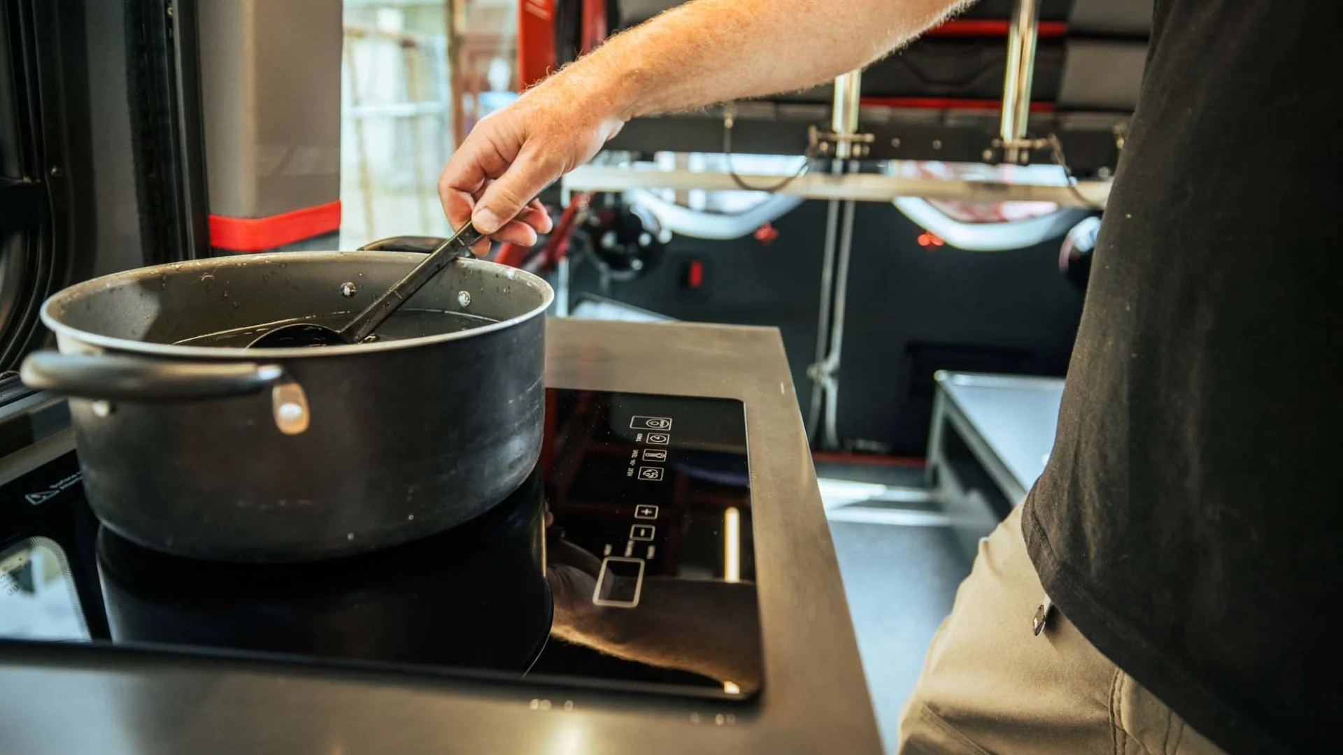 Person stirring contents in a pot on a modern induction cooktop in a sleek, compact kitchen setting.