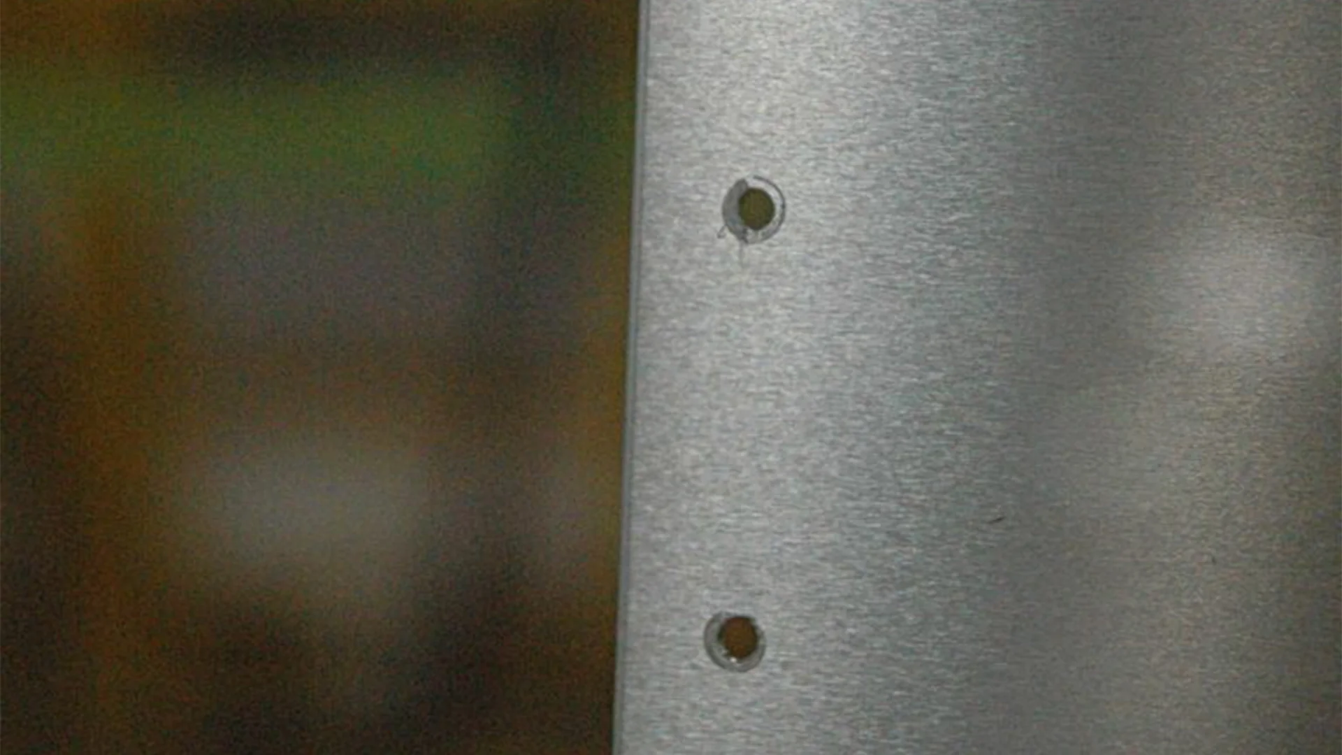Close-up of a metallic surface with three evenly spaced circular holes, against a blurred background.