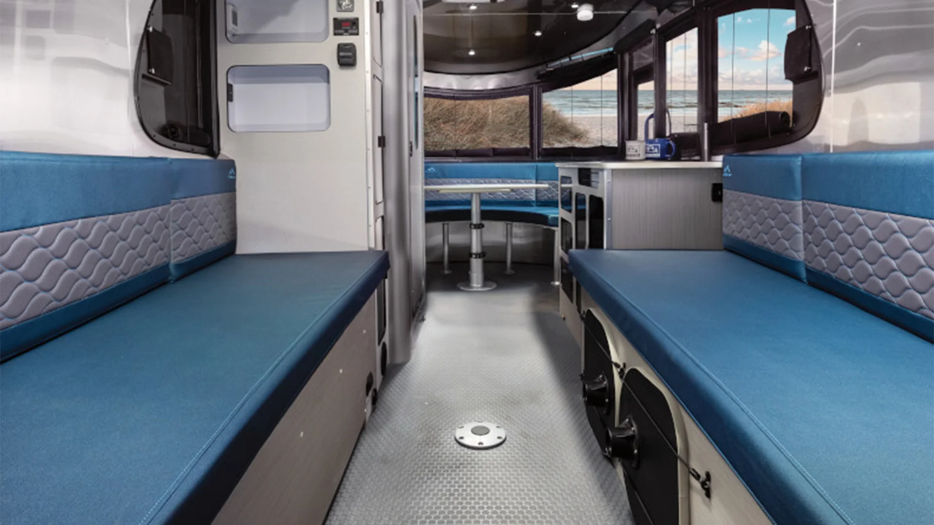Interior of a modern RV with blue seating, silver flooring, and large windows.