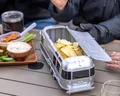 Airstream-shaped snack container holding chips on a table with wine, food platter, and people gathered around.