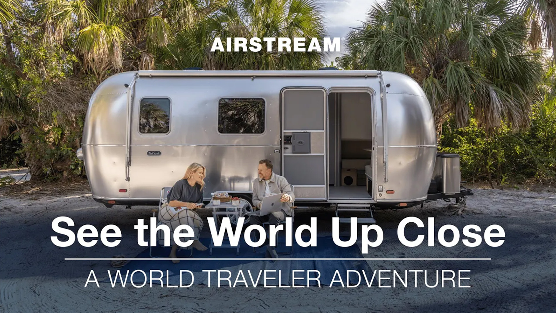 A couple sits outside a sleek Airstream trailer, surrounded by palm trees, with the text "See the World Up Close: A World Traveler Adventure."