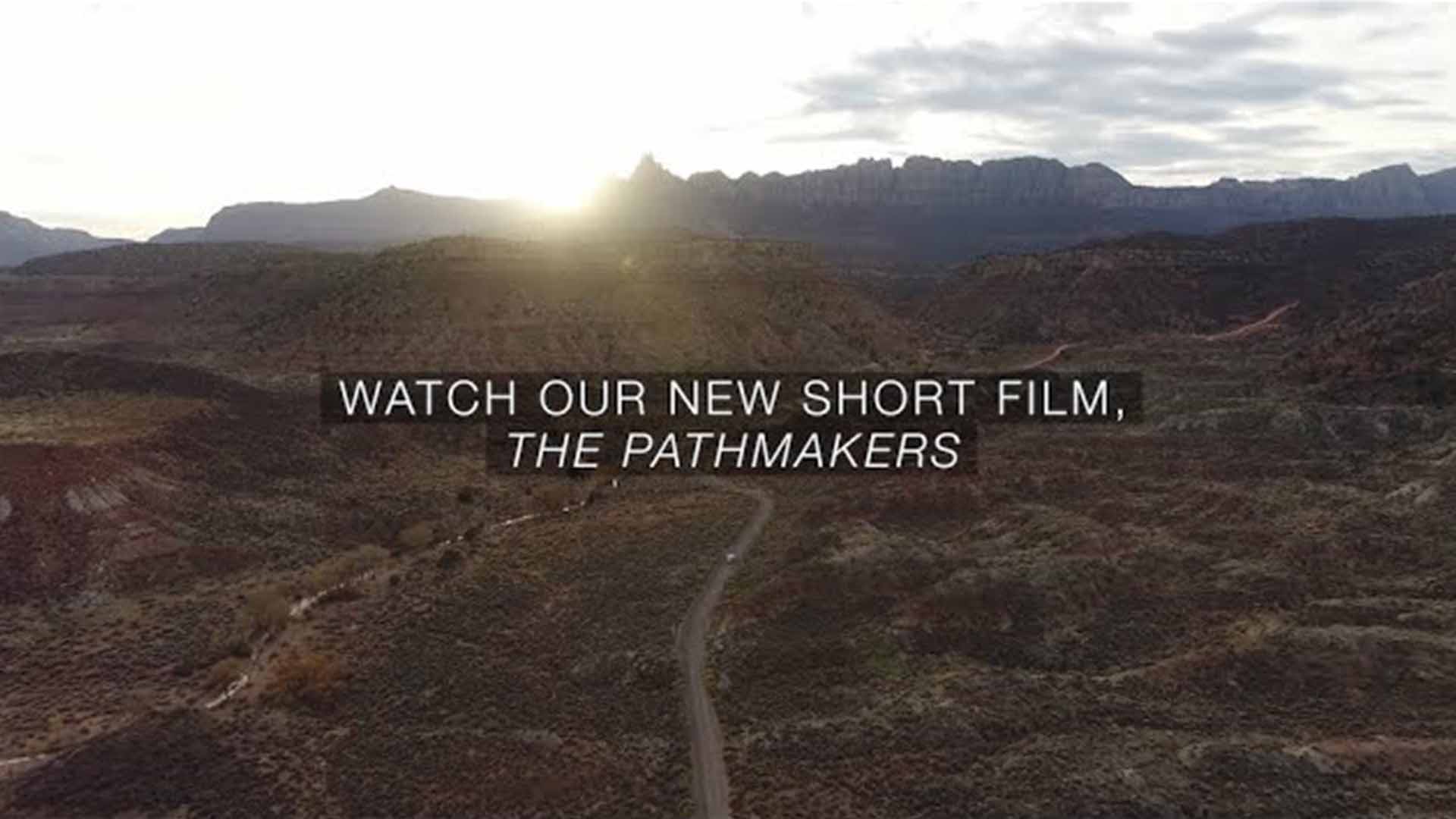 Landscape with mountains, a dirt path, and a sunset. Text reads, "Watch our new short film, The Pathmakers."