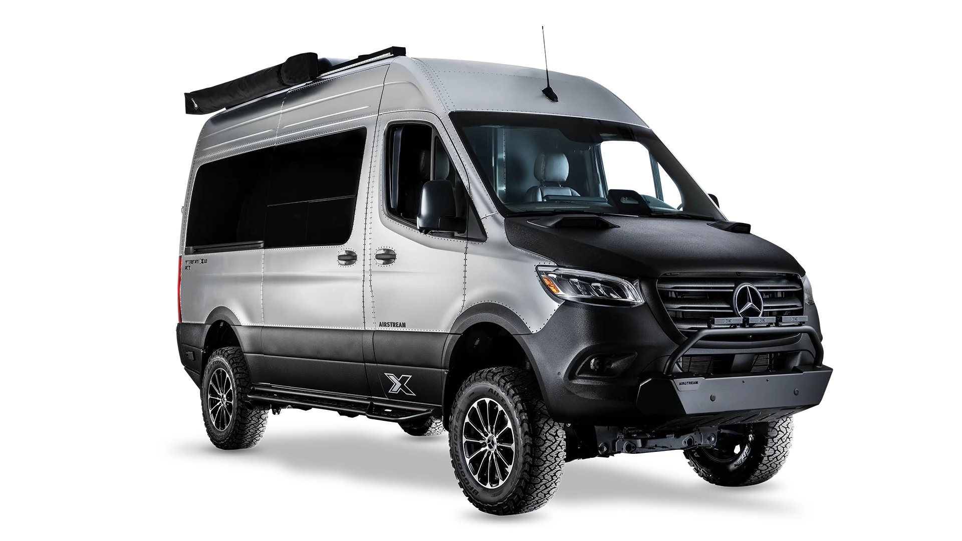 Silver and black camper van with rugged tires, side awning, and a sleek design, isolated on a white background.