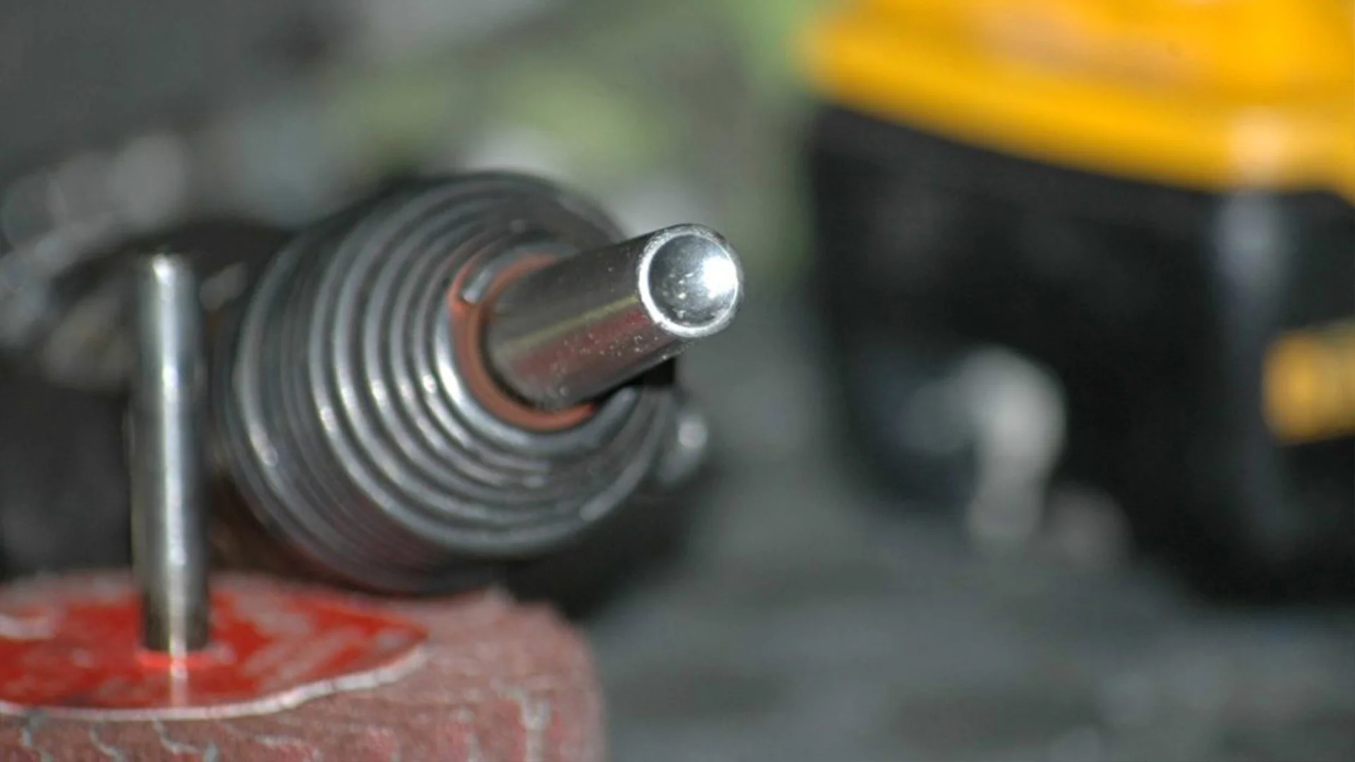 Close-up of a metal drill bit attached to a drill, with a blurred industrial background.