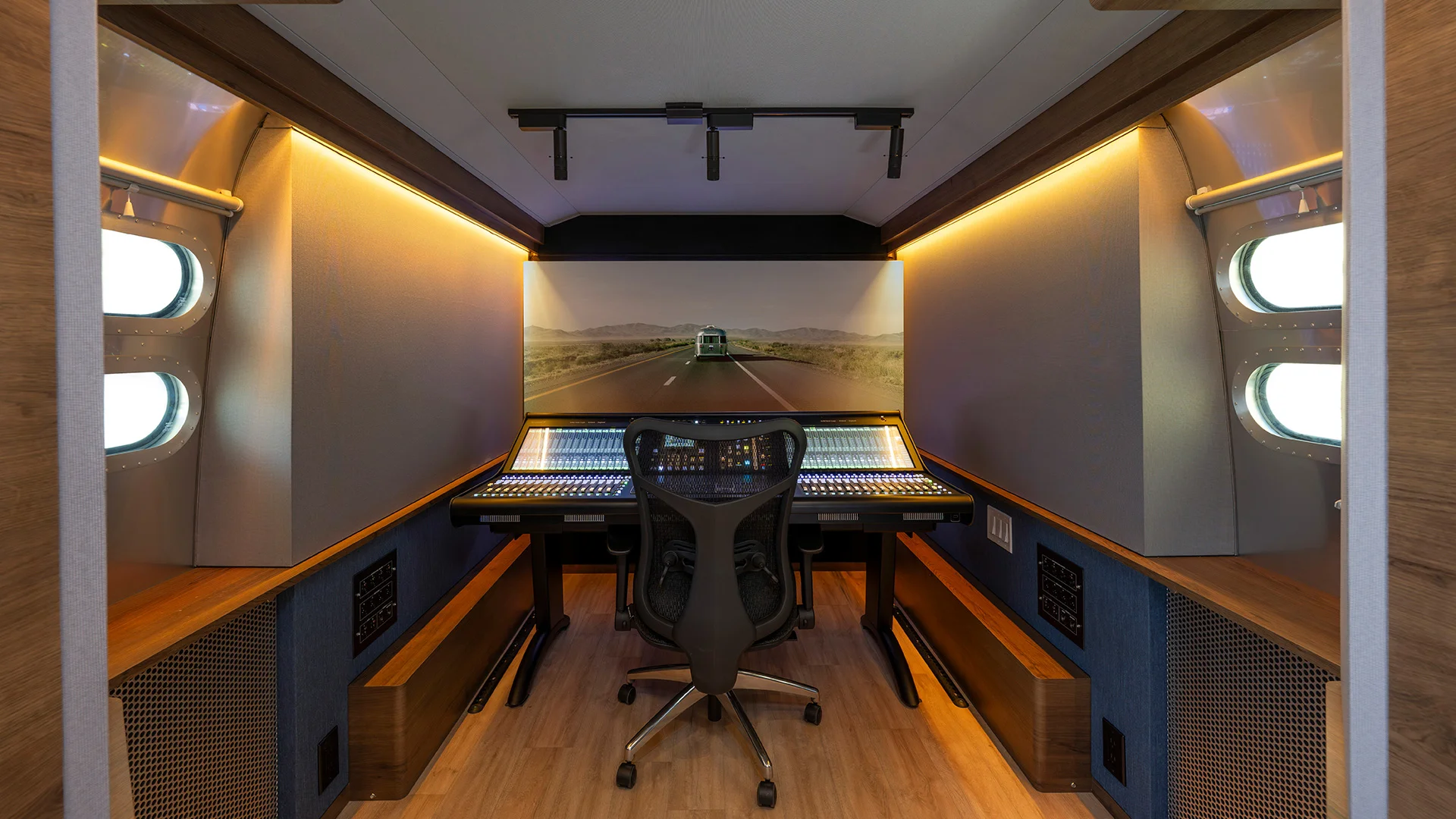 Interior of Airstream Sweetwater Studio Edition with a large mixing console, sleek chair, mood lighting, and a landscape image on the far wall.