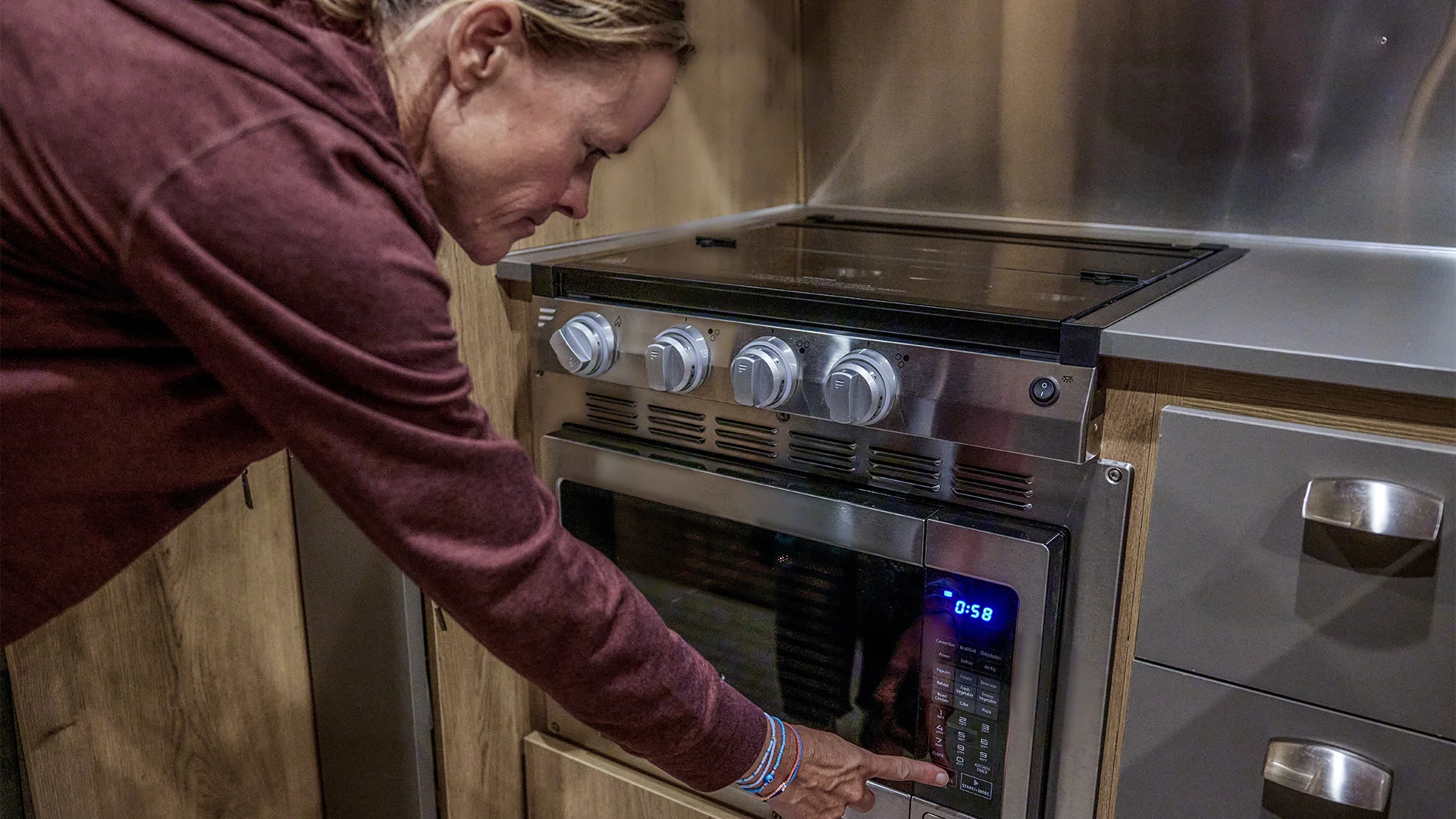 Person using a microwave with a digital display in a modern kitchen, pressing a button while leaning forward.