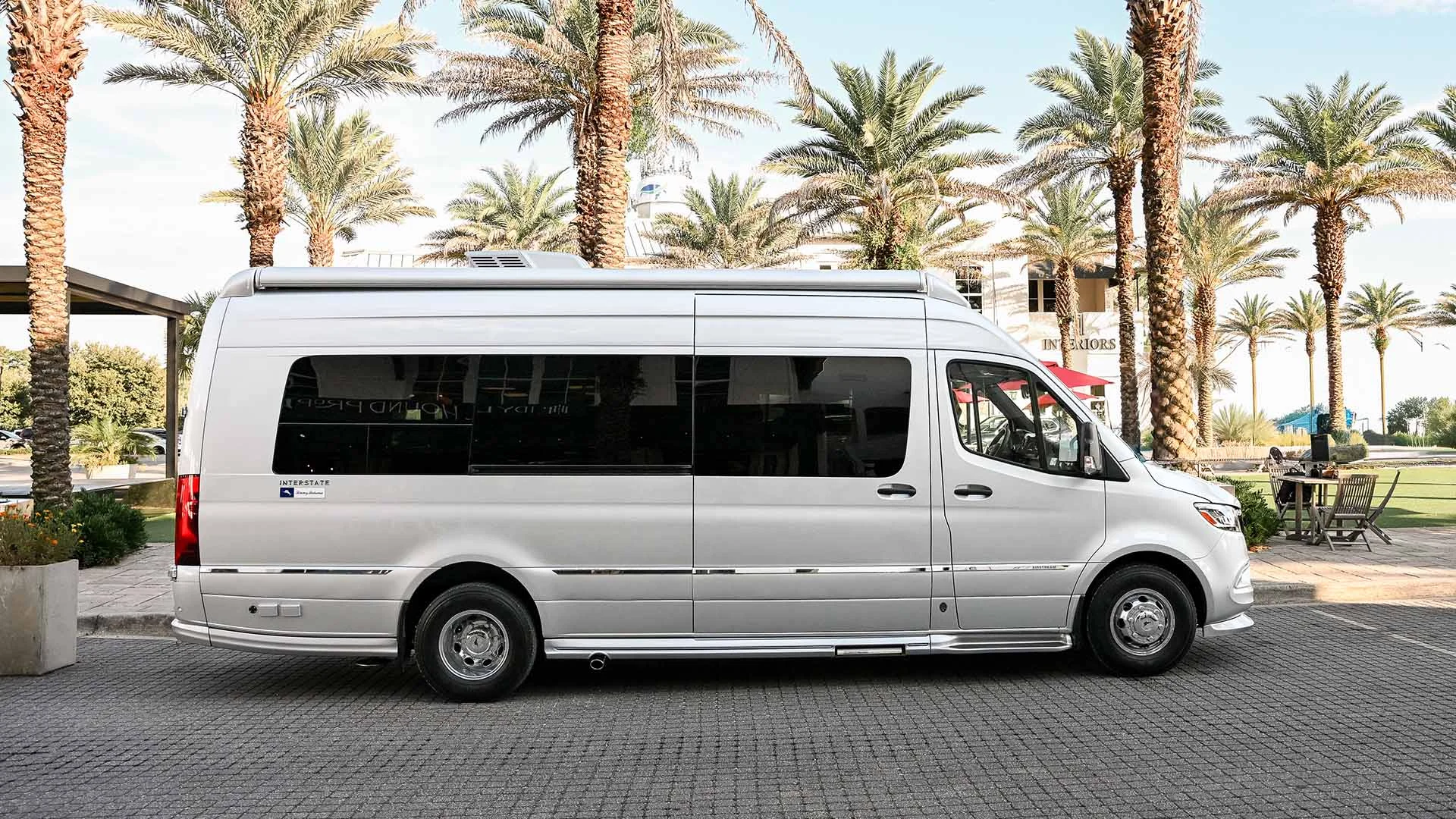 Silver van parked on a street lined with palm trees, under a clear sky.