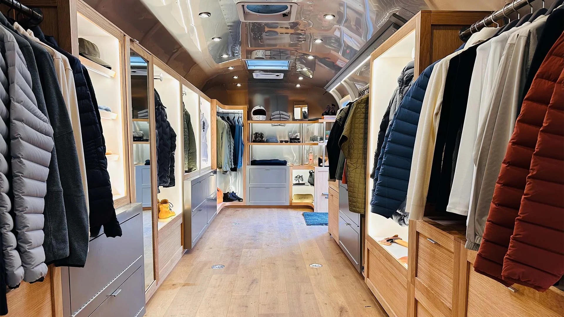 Interior of a modern trailer with wooden flooring, displaying rows of colorful winter coats and clothing on racks.