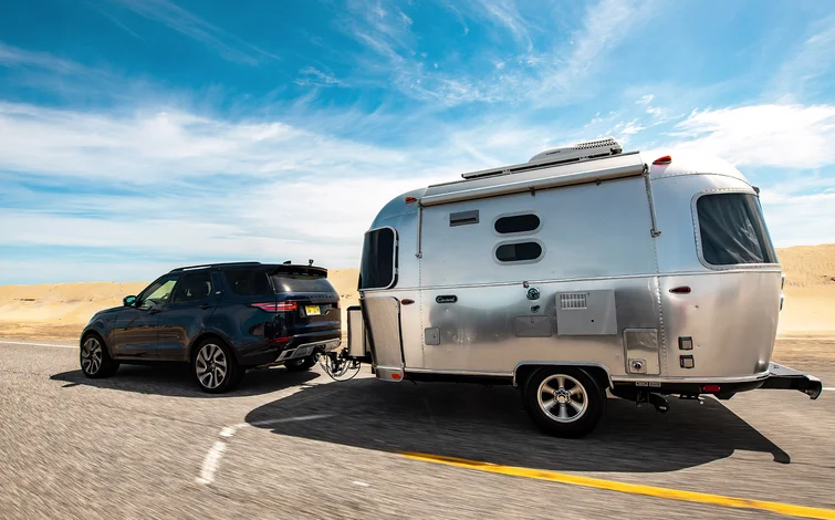 SUV towing a shiny silver caravan on a sunny desert highway, with clear blue skies overhead.