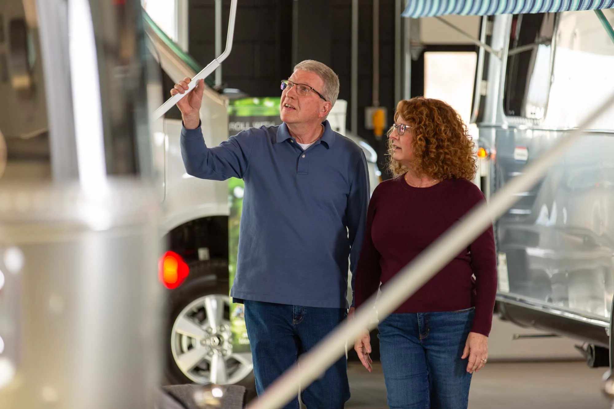 A man and woman examine a trailer at an indoor showroom, surrounded by RVs and camper vans.