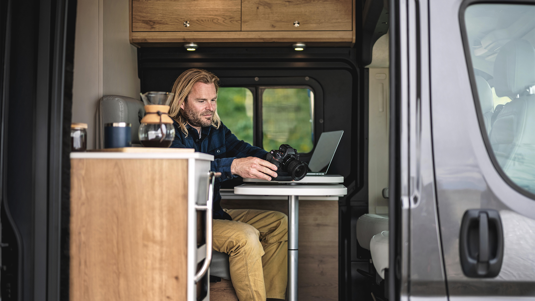 A man working on his computer and camera at the table while he is traveling in his Airstream Class B Rangeline Motorhome|Wi-fi map logo|speedtest logo|OpenSignal logo|A man working on his computer and camera at the table while he is traveling in his Airstream Class B Rangeline Motorhome