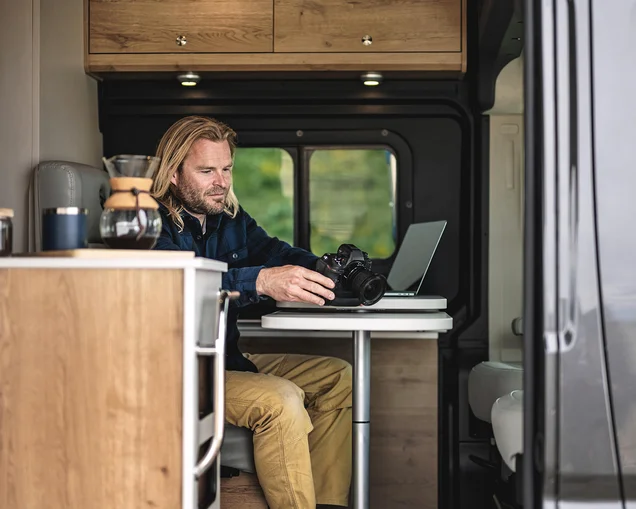 A man working on his computer and camera at the table while he is traveling in his Airstream Class B Rangeline Motorhome|Wi-fi map logo|speedtest logo|OpenSignal logo|A man working on his computer and camera at the table while he is traveling in his Airstream Class B Rangeline Motorhome
