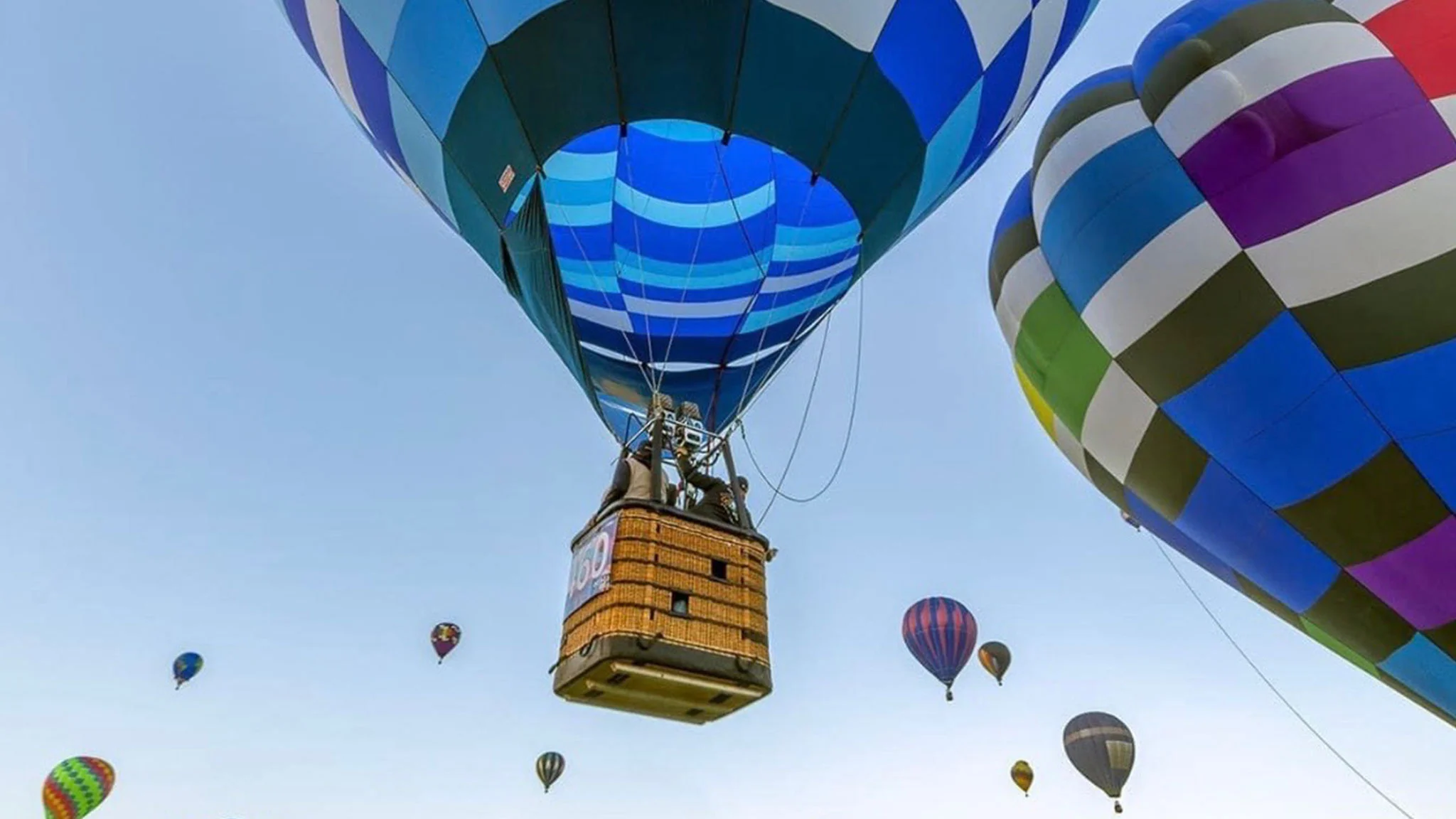 Colorful hot air balloons floating in a clear blue sky, with a focus on a large blue and black balloon in the foreground.