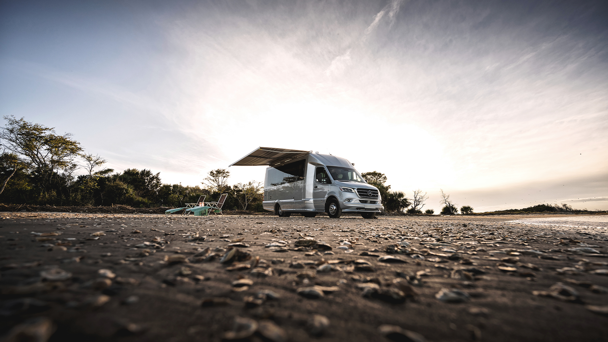 An Airstream Atlas Touring Coach parked on a beach and campers have out the awning.|AIRMKT-2023-Battery-Package-Diagram|AIRMKT-2023-Inverter-Capacity-Diagram|An Airstream Atlas Touring Coach parked on a beach and campers have out the awning.