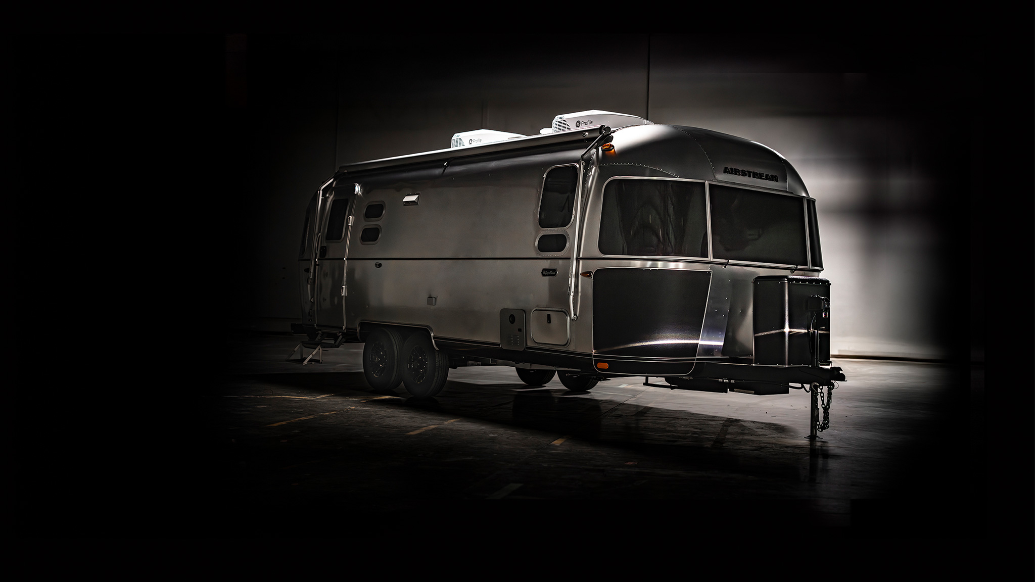 A sleek, silver Airstream trailer on display against a dark background, highlighting its modern design and polished exterior.