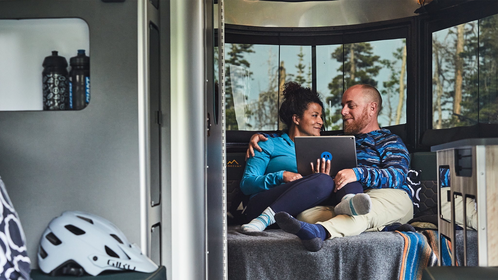 Two campers sitting on the bed of an Airstream Basecamp travel trailer watching their tablet.|A vintage photo from an Airstream on set of the television show The Troubleshooters.|A man sitting on the couch of an Airstream flipping through shows and movies on a tv.|A vintage image of a man standing next to his Airstream travel trailer with a video camera on a tripod.|Two campers sitting on the bed of an Airstream Basecamp travel trailer watching their tablet.