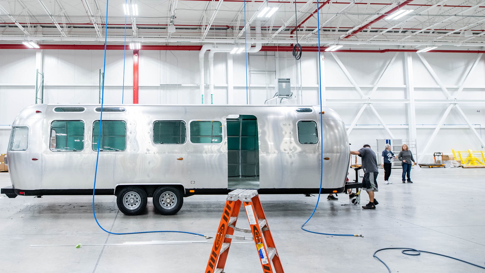 Airstream employees working on the shell of an Airstream Globetrotter travel trailer.|Two Airstream employees working together to rivet an Airstream travel trailer together.|A man and woman Airstream employee laughing while they work in the Airstream Class B Motorhome plant.|Two Airstream employees working together to build the shell of an Airstream travel trailer in Jackson Center, OH.|An Airstream employee checking the quality of an Airstream travel trailer.|Two Airstream employees work together to build apps to improve Airstream quality.|An Airstream employee watching a training video on a kiosk at the Airstream facility.|Airstream Class B Motorhomes being built in the Touring Coach facility in Jackson Center, OH|An Airstream travel trailer employee building a part of the iconic travel trailer.|Airstream employees working on the shell of an Airstream Globetrotter travel trailer.