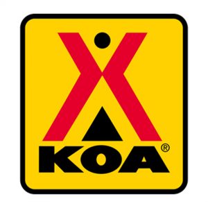 Yellow square logo with a red tent-like "X" and a small circle above it. The letters "KOA" are below the "X" in bold black font.