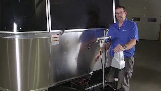 A person in a blue shirt stands beside a shiny trailer, demonstrating a connected device on a stand in an indoor setting.