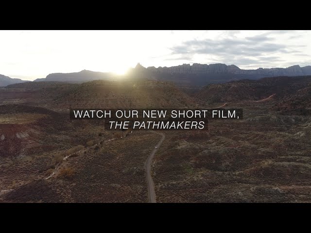 Aerial view of a scenic desert landscape at sunset with text overlay: "Watch our new short film, The Pathmakers."