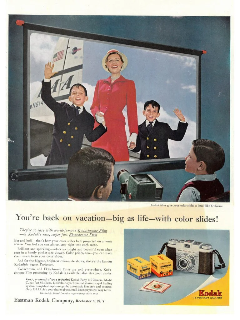 A smiling woman and two boys in sailor outfits wave in front of a projected color slide image, with Kodak camera and film boxes displayed below. Text promotes Kodaks color slides for vacation memories.