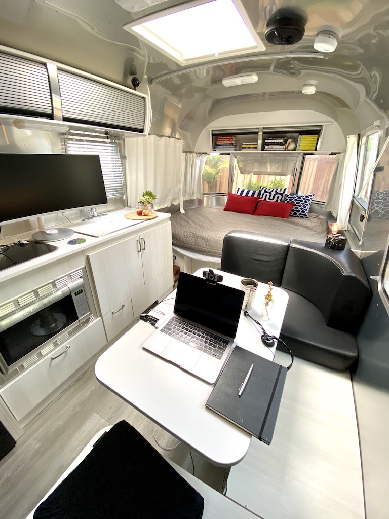 Interior of a modern RV with a table, laptop, couch, bed, and kitchen area, featuring a skylight above.