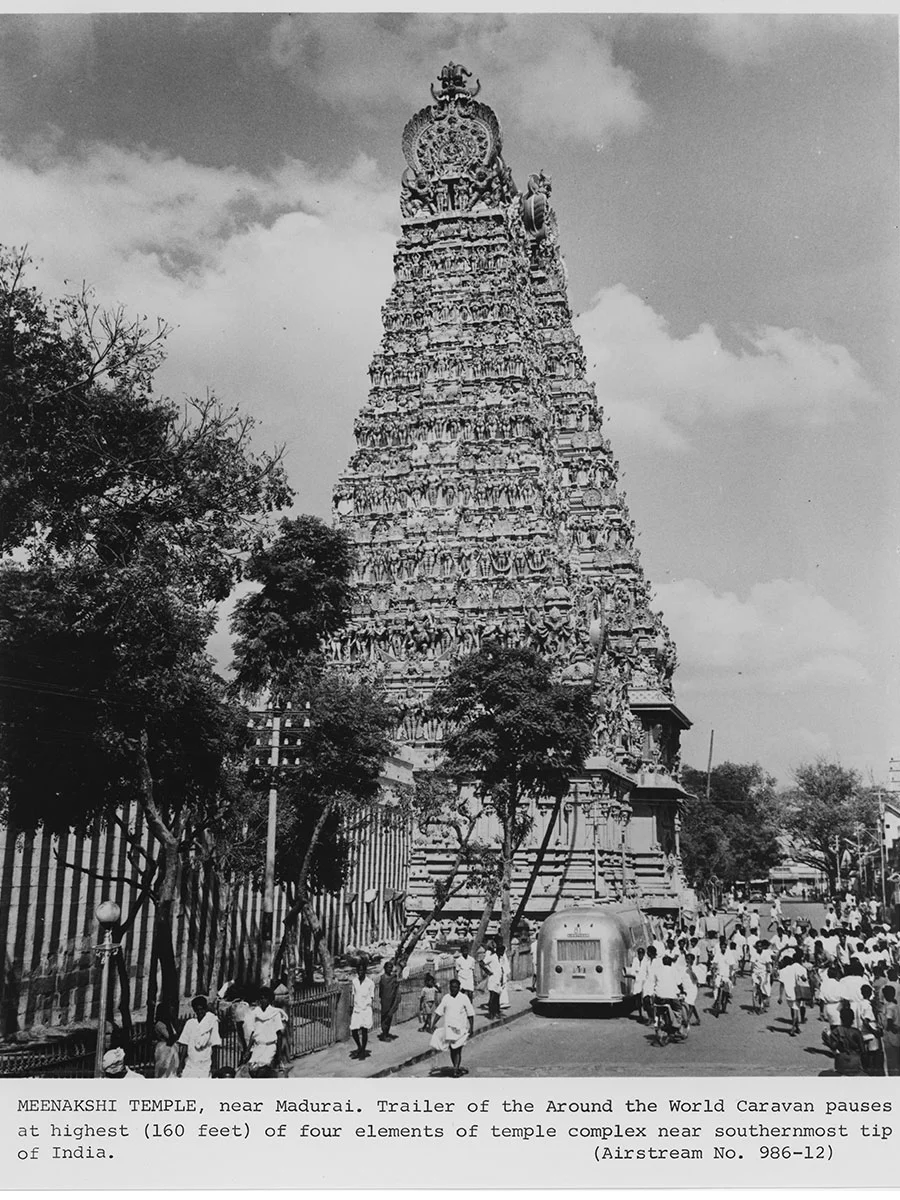 A black and white photo of the Meenakshi Temple in Madurai, showing its intricate tower, with people and a trailer nearby.