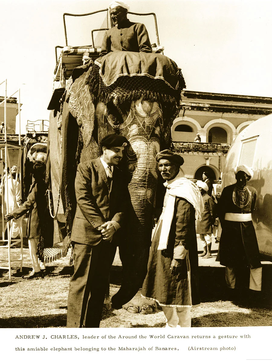 A group of people stand beside a decorated elephant with a rider, in front of a historic building, posing for a photo.